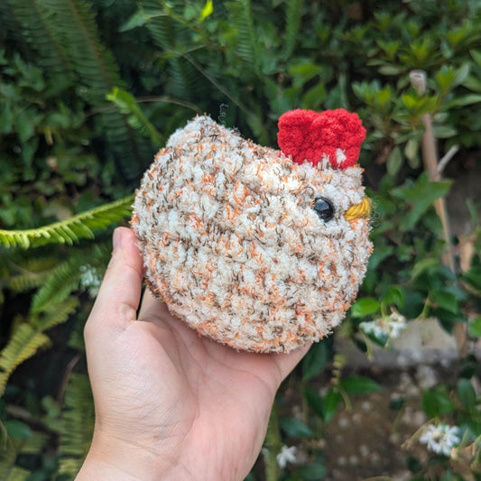 A round crocheted chicken in tweed colouring with red head feathers