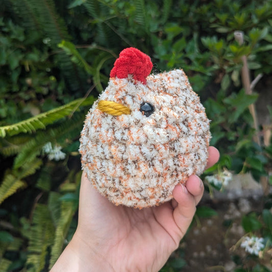 A round crocheted chicken in tweed colouring faces the camera
