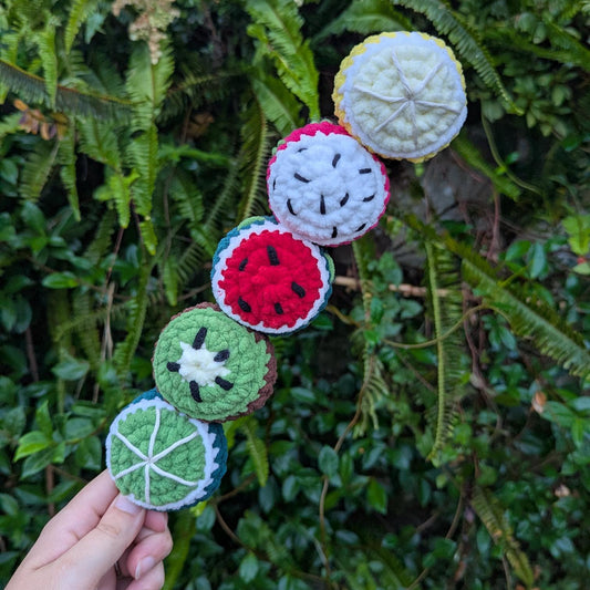 5 crocheted fruit balls on a green foliage backdrop.