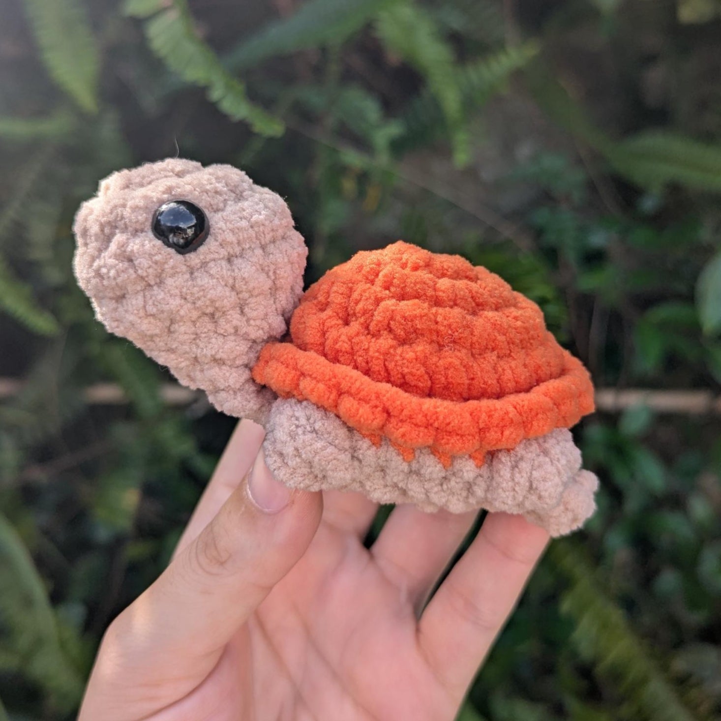 A crocheted plush turtle with tan body and orange shell