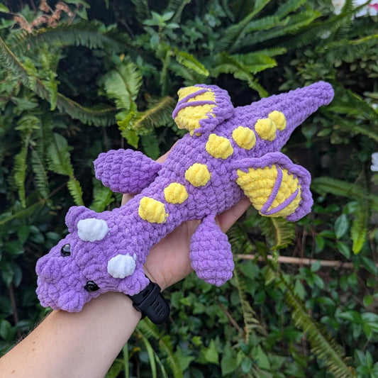 A purple crocheted dragon with yellow spikes and wing details